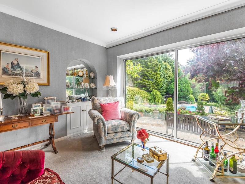 Natural light floods in through the glass, with the established gardens and pool as a backdrop
