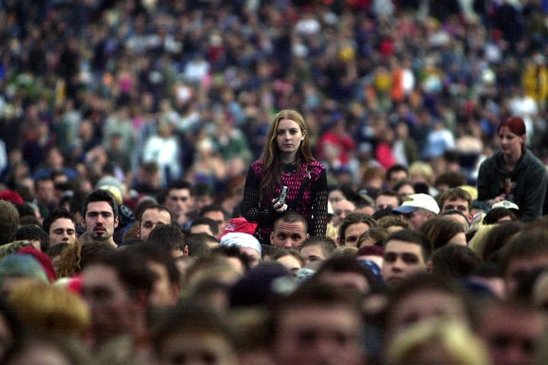 Music fans are packed together in front of the main stage at Leeds Festival while a girl tries to get the best view from someones shoulders.