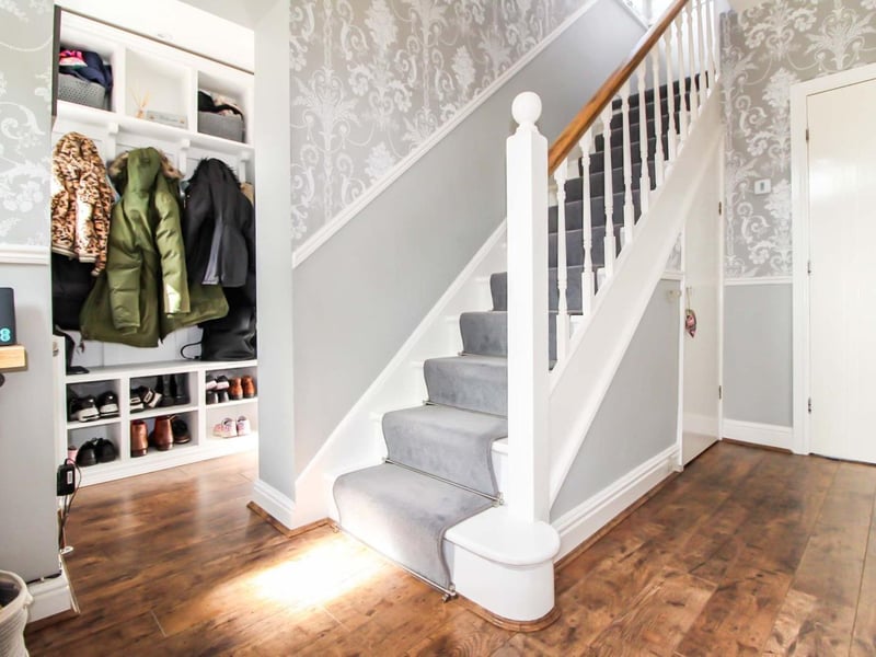 Enter into the hallway, decorated in light grey tones and a hardwood floor. To the left is a useful built in storage area and downstairs WC.