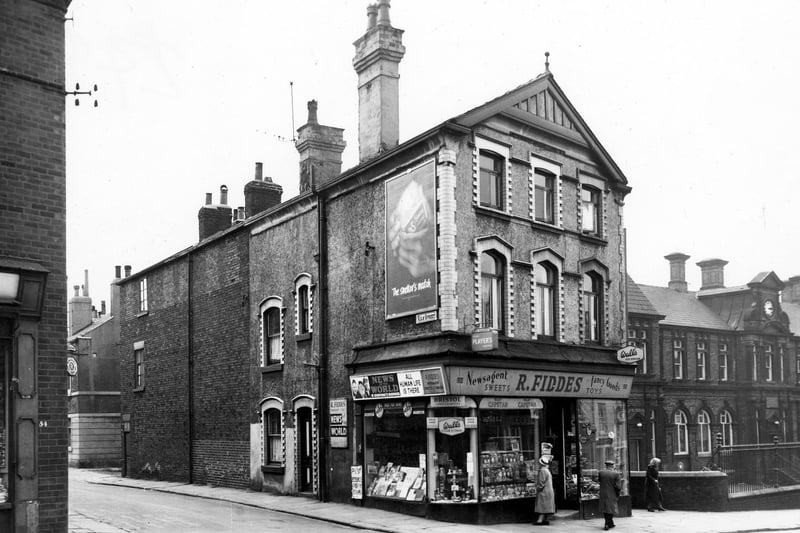Beeston Road and the junction with Kiln Stree in July 1964.. A woman looks in the window of R. Fiddes, newsagents. To the far right is Hillside School, originally Beeston Hill Board School, a mixed school.
