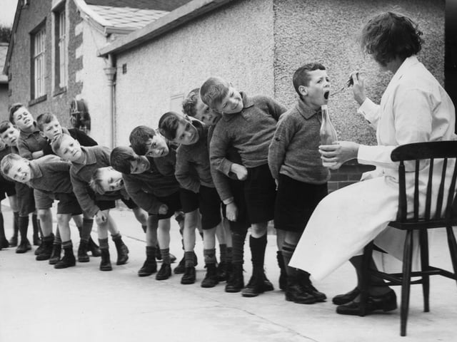 Children from Bradford lining up for a dose of medicine during a holiday at Morecambe. Year unknown.