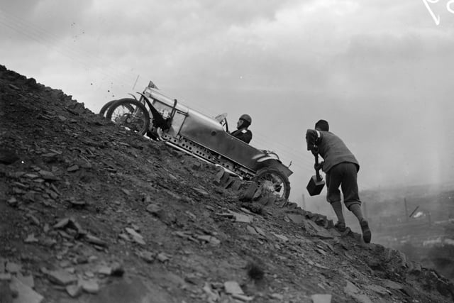 A supporter takes a large mallet to help a competing driver up a steep, shale-covered slope in hill climbing event at Freak Hill near Bradford in May 1927.