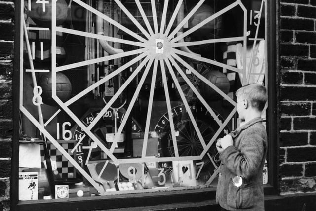 A boy looking a sports shop window in Bradford, where the tape used to prevent the window shattering has been arranged into the shape of a dart board in December 1939.