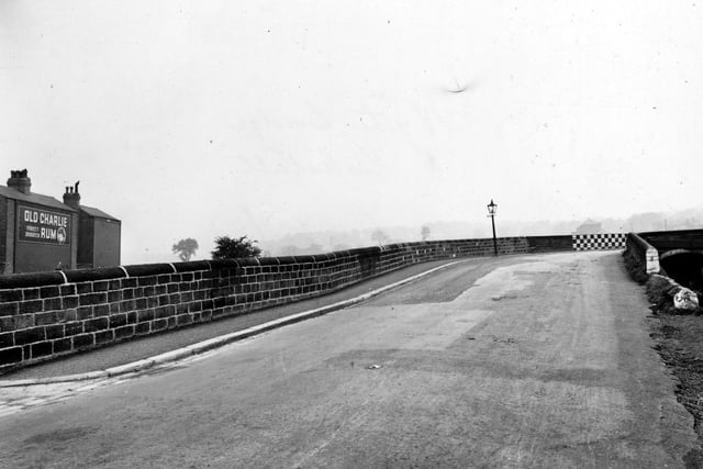 Wyther Lane towards the bridge over the Leeds & Liverpool Canal in October 1948. The bridge's wall is painted with black and white checks on the corner. An advertisement for Old Charlie's Jamaica Rum is on a house to the left.