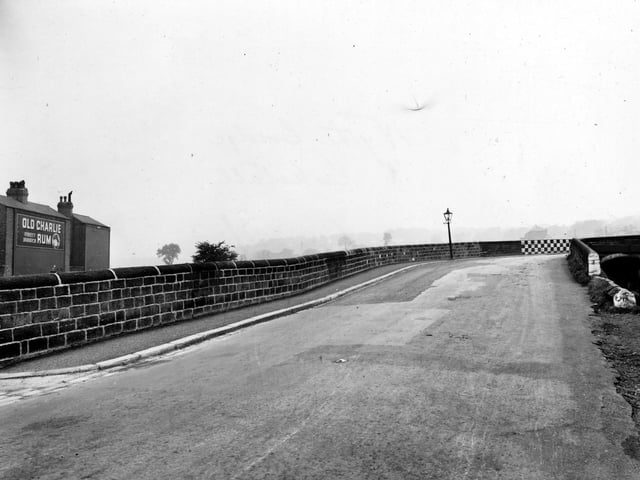 Wyther Lane towards the bridge over the Leeds & Liverpool Canal in October 1948. The bridge's wall is painted with black and white checks on the corner. An advertisement for Old Charlie's Jamaica Rum is on a house to the left.