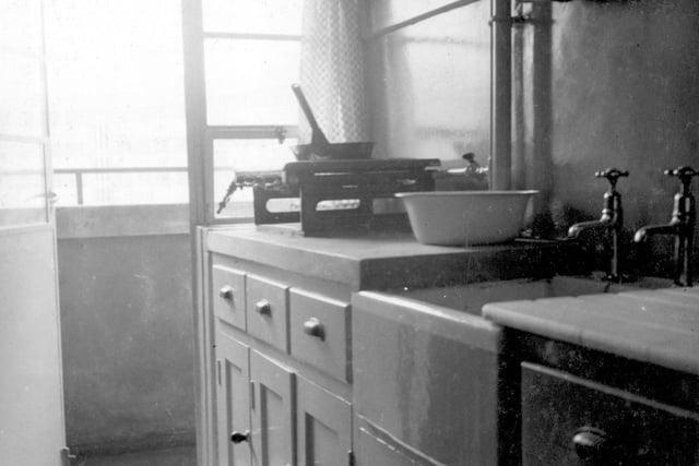 A kitchen at Quarry Hill Flats with a door opening on to the balcony. There are cupboards and drawers for storage. To the left of the sink is a gas 'griller', comprising a grill facility with gas rings for boiling or frying food on.