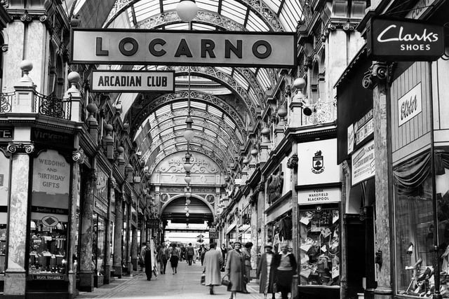 The County Arcade looking from the junction with Cross Arcade towards Briggate. On the left corner is Vickers gift shop selling silver, jewellery and watches. On the right, opposite, is a branch of Greenwoods menswear. Next right is the entrance to the Mecca Locarno Ballroom then Elster shoe shop.