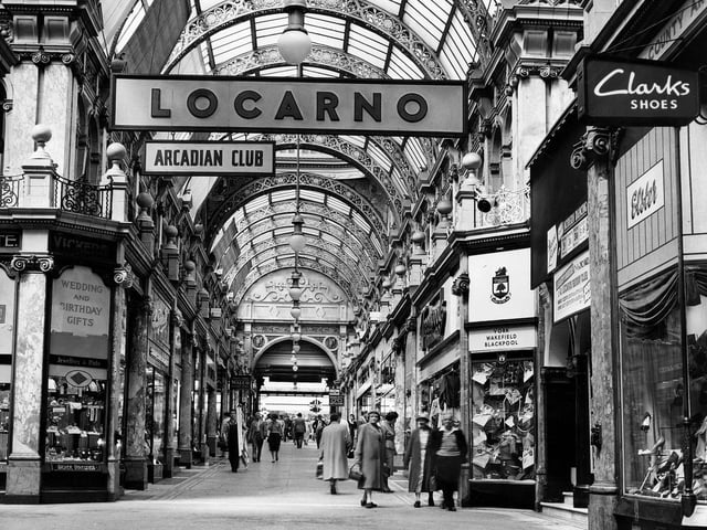The County Arcade looking from the junction with Cross Arcade towards Briggate. On the left corner is Vickers gift shop selling silver, jewellery and watches. On the right, opposite, is a branch of Greenwoods menswear. Next right is the entrance to the Mecca Locarno Ballroom then Elster shoe shop.