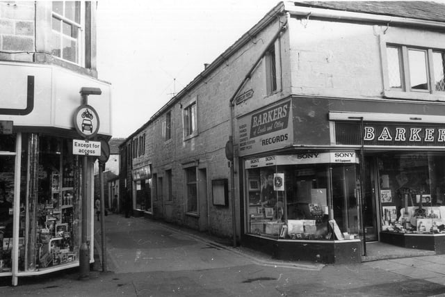 Kirkgate at the junction with Mercury Row. To the right of the junction is Barkers musical instruments and records . On the left, part of Bakers clothiers and drapers on Kirkgate can be seen. Along Mercury Row is U-Du-Save discount store.