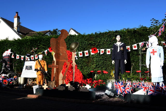 The display includes uniformed figures, flags, bunting, commemorative crosses, a First World War soldier silhouette and a cascade of poppies, with music playing in the background.