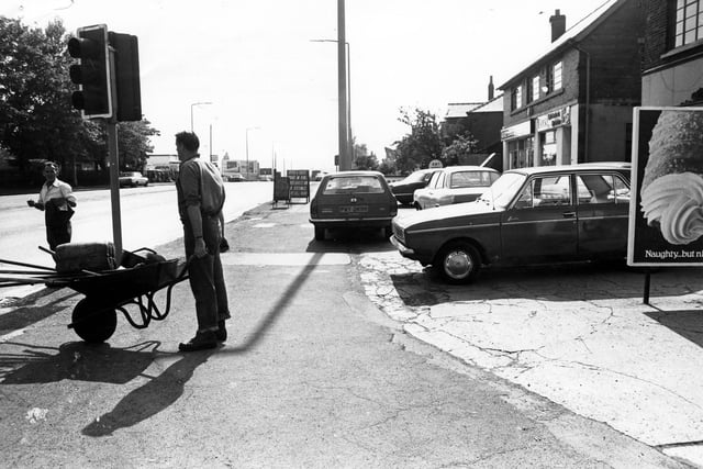 Dewsbury Road at the junction with Old Lane (foreground) in June 1980. A workman with a wheelbarrow of tools is seen and work on the road is in progress. The cameraman is standing with his back to Old Lane, looking south down Dewsbury Road, towards The White Rose Centre, and Morley. The Tommy Wass Public House is directly behind him at the other side of Old Lane.