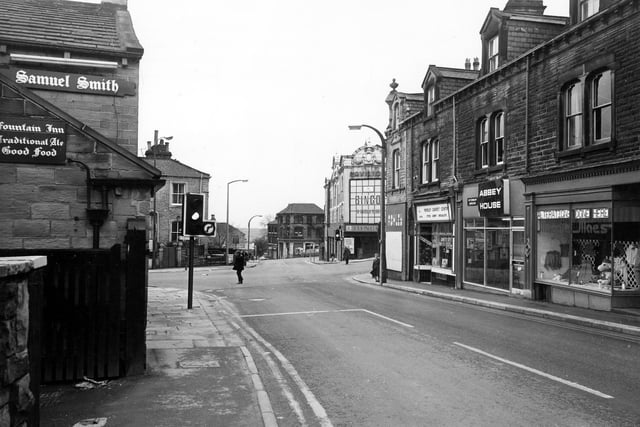 Fountain Street towards the junction with Queen Street, High Street, and South Queen Street ion October 1980. On the left is the Fountain Inn. On the right, shops on Fountain Street include Abbey House veterinary surgery and Morley Carpet Centre, with James Ashley, menswear, boarded up on the corner. Across the road is the Pavilion Bingo and Social Club.