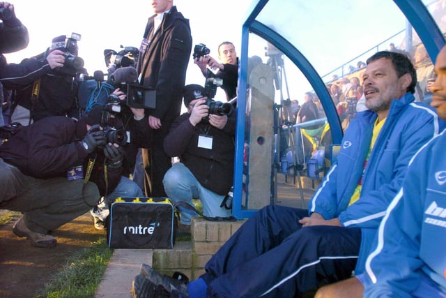 Socrates takes his place on the bench ahead of kick-off as the press pack takes photos.