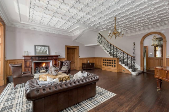The Scottish splendour of this property includes an interior with rooms like this, featuring huge fireplaces. There's an ornate feature staircase, decorative ceiling and wood panelling to the walls.