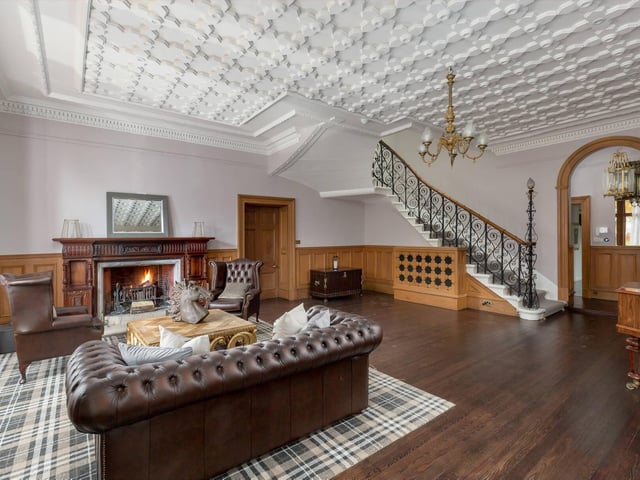 The Scottish splendour of this property includes an interior with rooms like this, featuring huge fireplaces. There's an ornate feature staircase, decorative ceiling and wood panelling to the walls.