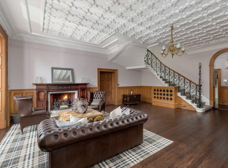 The Scottish splendour of this property includes an interior with rooms like this, featuring huge fireplaces. There's an ornate feature staircase, decorative ceiling and wood panelling to the walls.