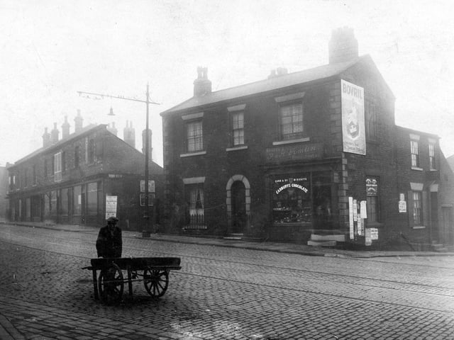 Burley Street in October 1928. Shop and house, premises of F and H Tomlin, confectioners. 'Bovril' poster on wall. On the left, row of shops, to the right, junction with St. Andrews Street. Broad cobbled road with tramlines.