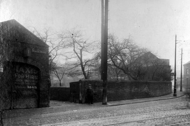 Armley Road at the junction with Crab Lane in February 1929. A man is outside the entrance to 'Taxis for hire', owned by Jack Naylor. Tram stop on the corner with sign on lamp post stating 'Tramway fare Stage'. Cobbled road with tramlines along Armley Road.