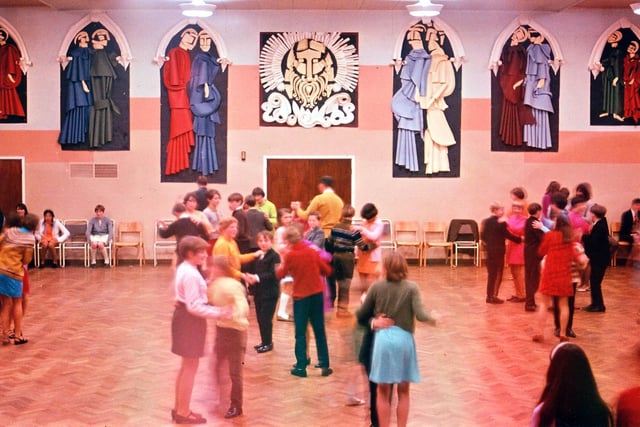 A Christmas party is in full swing for the second year forms in the school hall. The walls are decorated for Christmas with stained glass effect windows. The religious figures are clothed in robes of rolled and curled paper giving a 3-D effect.