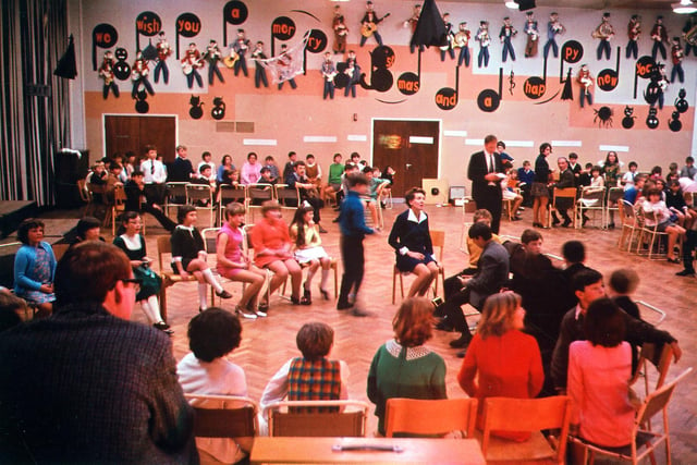 Pupils taking part in a Christmas Party held in the main hall in December 1968. They appear to be playing party games. The hall has been decorated with a music theme including musical notes and guitarists.