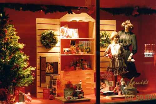 Christmas displays in one of the windows. The background resembles a pine furniture unit and ladies' perfumes and gifts are arranged on the shelves and around the Christmas tree. The 'halo' hairstyle of the adult mannequin and tiered skirts of both would be consistent with a late 1970s date.