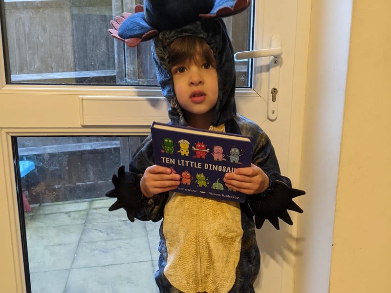 Little three-year-old Sam has dressed up as a dinosaur while holding his favourite book, 'Ten Little Dinosaurs'.