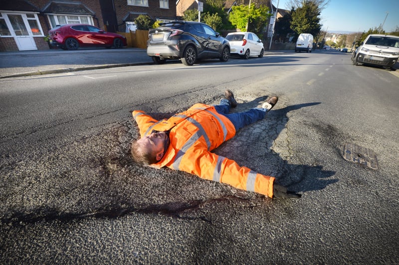Andrew Crotty lying on top of a giant pothole in Buckhurst Road, Bexhill. SUS-210704-091114001