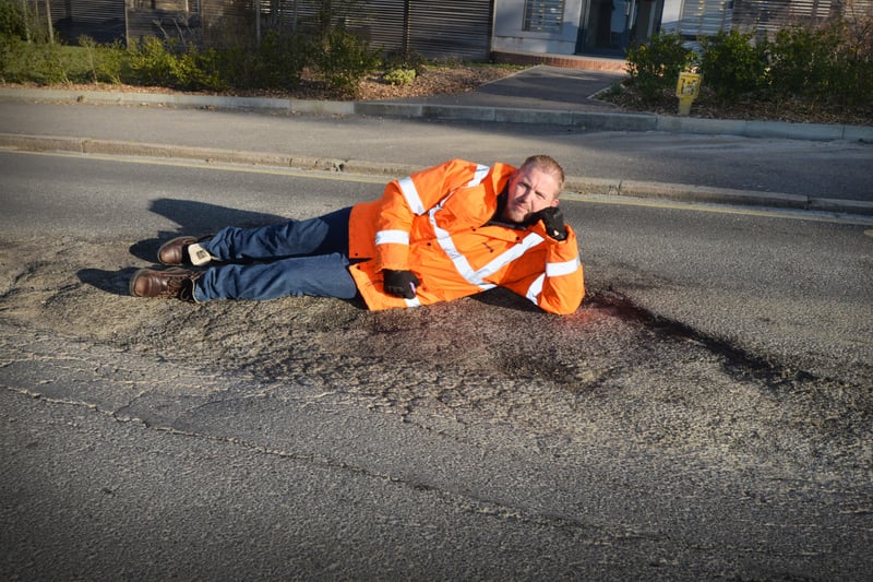 Andrew Crotty lying on top of a giant pothole in Buckhurst Road, Bexhill. SUS-210704-091114001