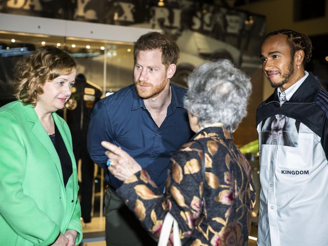 The Silverstone Experience chief executive Sally Reynolds, Prince Harry and Lewis Hamilton listen to Lady Christabel Watson talk about her old racing suit on display
