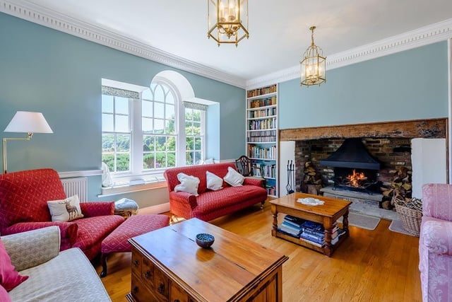 A lovely double aspect sitting room with an inglenook fireplace, two sash windows and a further large arched window overlooking the garden and views