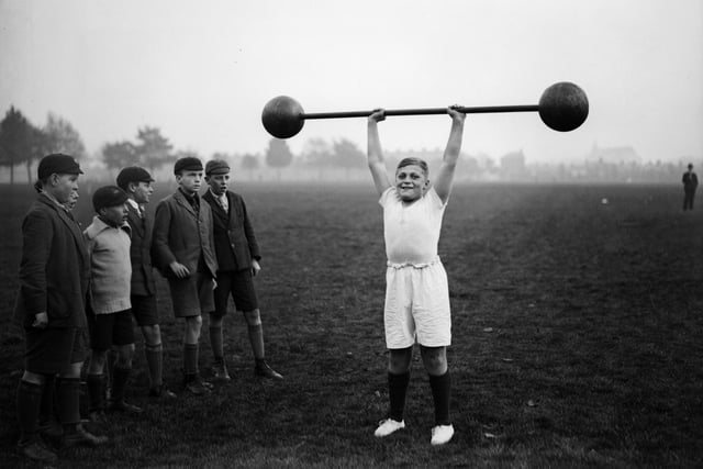22nd October 1931: Northampton schoolboy William Albert Tuckley raises a dumb-bell weighing 110 pounds above his head, to the amazement of his classmates. Eleven-year-old Tuckley is being trained by Mr French, weightlifting champion of Northamptonshire and Buckinghamshire. (Photo by Fox Photos/Getty Images)