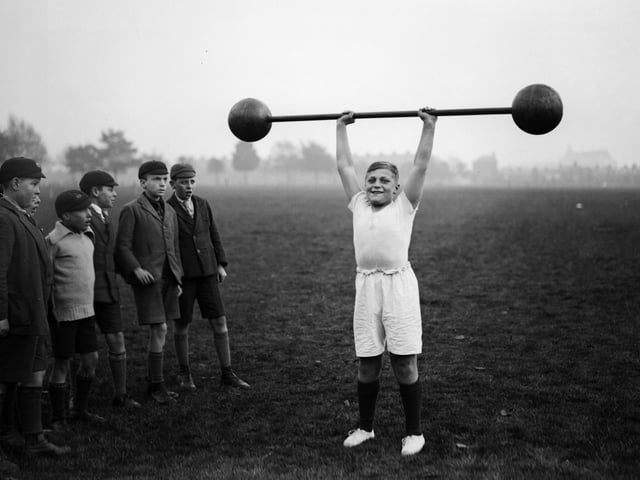 22nd October 1931: Northampton schoolboy William Albert Tuckley raises a dumb-bell weighing 110 pounds above his head, to the amazement of his classmates. Eleven-year-old Tuckley is being trained by Mr French, weightlifting champion of Northamptonshire and Buckinghamshire. (Photo by Fox Photos/Getty Images)