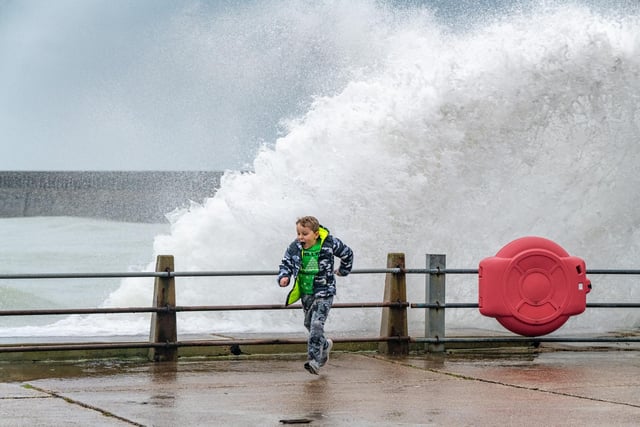 A boy runs for cover  as waves slam against the harbour wall at Newhaven