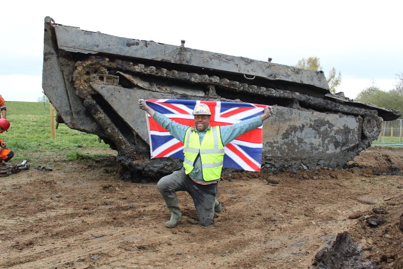 Daniel Abbott kneeling with the flag in front of the tank (Credit: Cathi Elphee)
