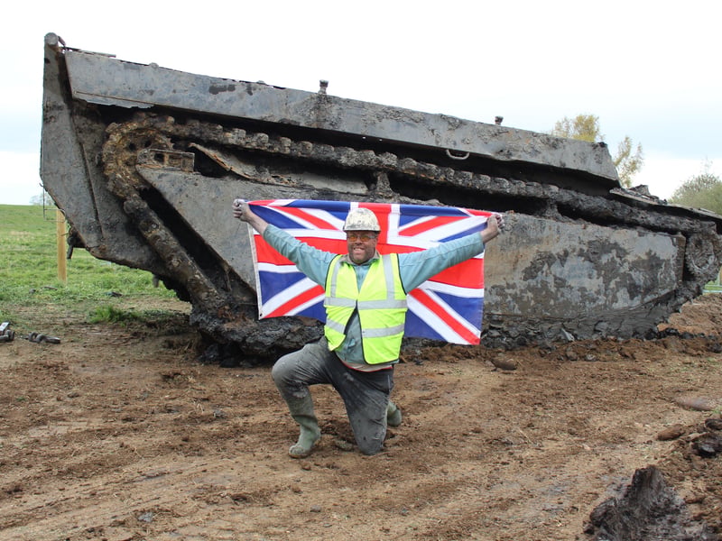 Daniel Abbott kneeling with the flag in front of the tank (Credit: Cathi Elphee)