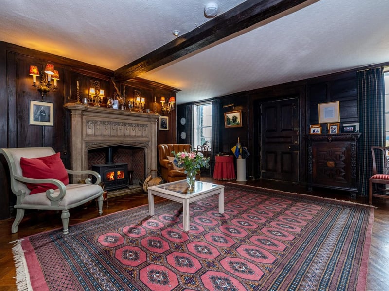 The entrance hall, featuring polished wood floor, panelled walls (dated 1711), beamed ceiling and stone fireplace.