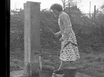 Nora Edginton using the pump on The Green, Dodford.