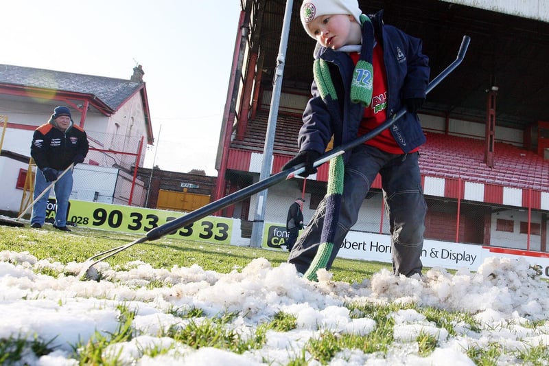 Brendan Young attempts to clear the snow from the pitch at Cliftonville FC