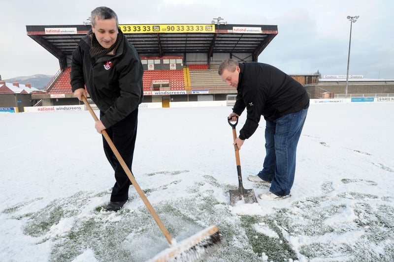 Chairman Stephen Bell and Vice Chairman Ronnie Millar attempt to clear the snow off the pitch before their game against Ballymena United