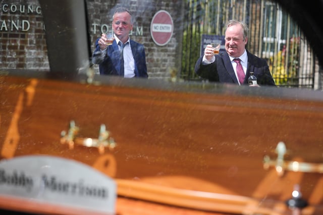 Actors Paddy Jenkins and Damon Quinn join family and friends to raise a toast outside Roselawn Cemetery in Belfast as the hearse arrives during the funeral of actor BJ Hogg