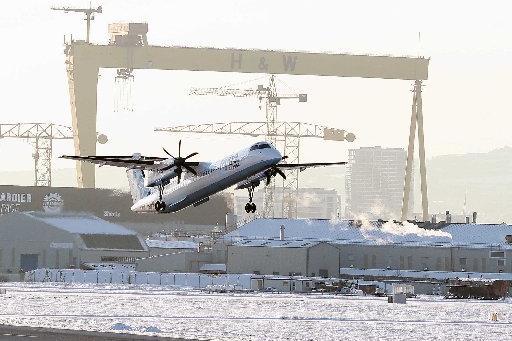 A plane takes off at George Best Belfast City Airport amidst a snowy backdrop of the Harland and Wolf cranes.
