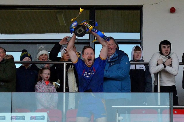 Captain Neil Forester lifts aloft the trophy as Steelstown players look on from the pitch.