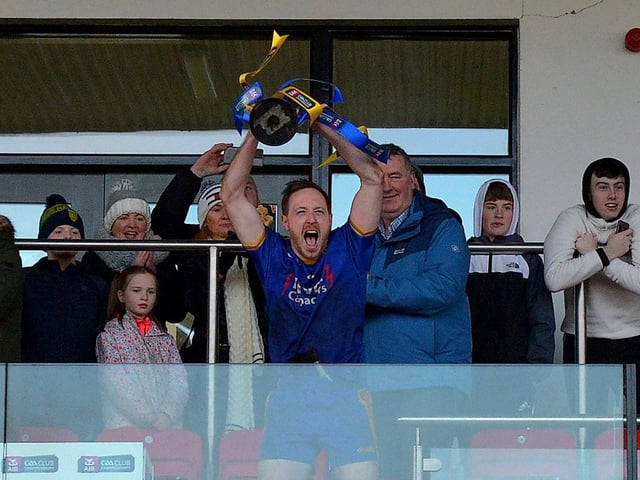 Captain Neil Forester lifts aloft the trophy as Steelstown players look on from the pitch.