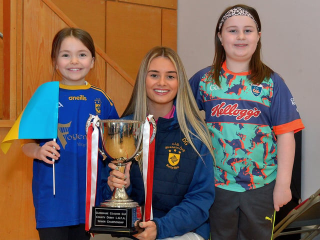 Pupils Grace Callan and Amelia Doherty, P5 pupils at St Patrick’s Primary School Pennyburn, pictured with Steelstown Brian Og’s ladies player Ella-Rose Sainsbury and the Derry Ladies Senior Championship trophy during a visit to the school on Friday morning last. Photo: George Sweeney. DER2208GS – 081