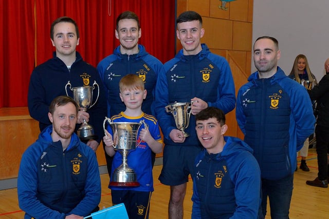 Caoimhan Toner, P5 pupil at St Patrick’s Primary School Pennyburn, pictured with Steelstown Brian Og’s players Ciarán Flanaghan, Dermot McBride, coach, Morgan Murray, Garth Logue, Neil Forester, captain and Jason McAleer with the Derry, Ulster and All Ireland Intermediate Football Championship trophies during a visit to the school on Friday morning last. Photo: George Sweeney.  DER2208GS – 083