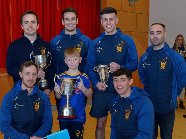 Caoimhan Toner, P5 pupil at St Patrick’s Primary School Pennyburn, pictured with Steelstown Brian Og’s players Ciarán Flanaghan, Dermot McBride, coach, Morgan Murray, Garth Logue, Neil Forester, captain and Jason McAleer with the Derry, Ulster and All Ireland Intermediate Football Championship trophies during a visit to the school on Friday morning last. Photo: George Sweeney. DER2208GS – 083