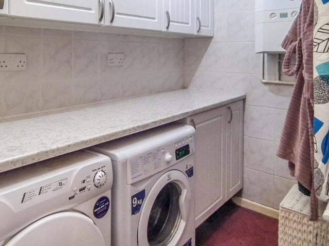 Utility room, with a range of wall and base units with coordinating work surfaces. There is plumbing for a washing machine, an area for a dryer and a wall mounted boiler. With access to the WC.