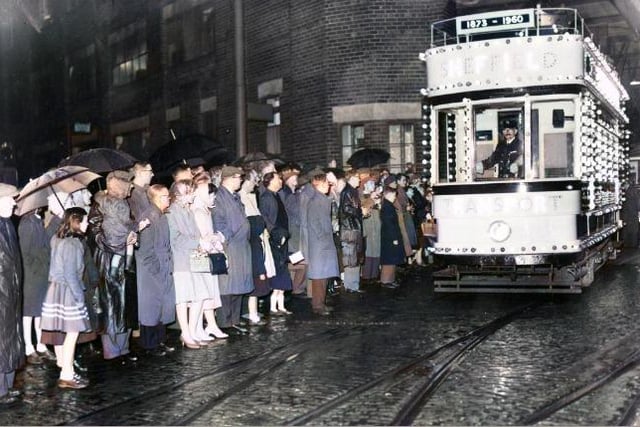 Sheffield residents watch in the rain during the city's 'Last Tram' parade in 1960. The AI has brought out colour in their clothing