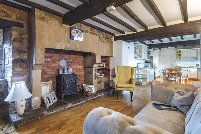Featuring a Derbyshire stone fireplace with exposed stone head, side supports and raised stone hearth housing an electric coal effect cast iron stove, light oak flooring, radiator and open space leading into breakfast kitchen.