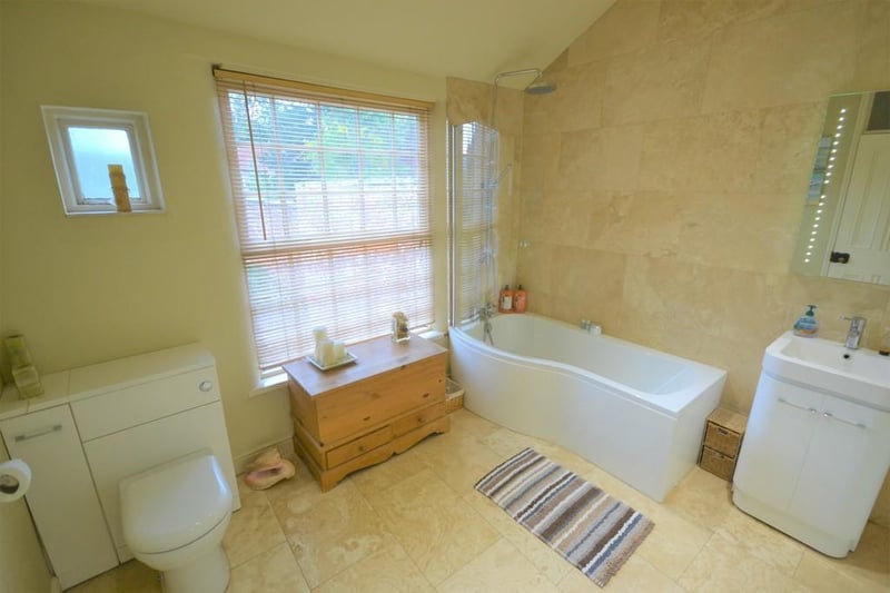 A large family bathroom situated on the first floor -  a white 3 piece suite incorporating a P shaped bath with curved screen and dual chrome shower heads over, wash basin with chrome mixer tap inset to a white vanity cupboard and matching low flush w.c.